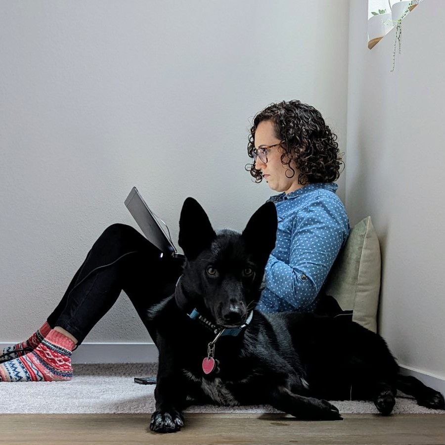 Kimberly sitting on the floor typing her novel next to a black dog named Koda